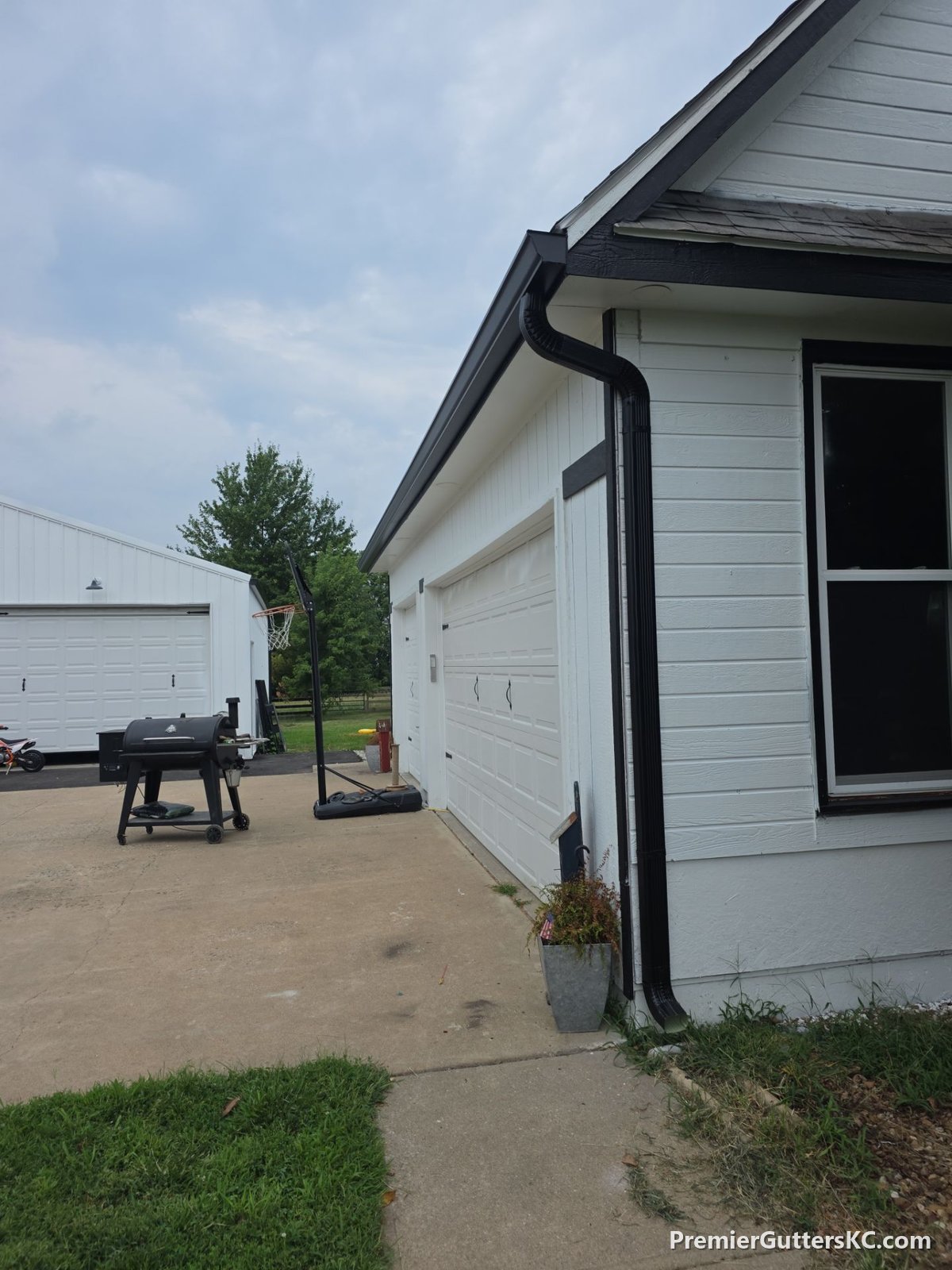 Black seamless gutters and downspout on a white farmhouse and attached garage in Napoleon, Missouri