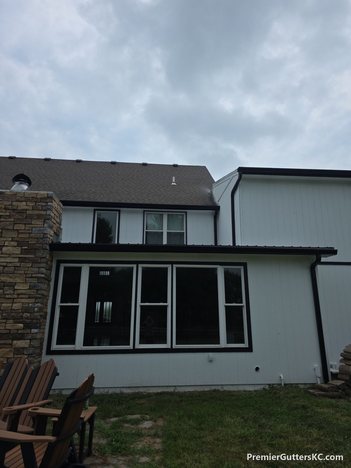 Black seamless gutters on a two-story board-and-batten home with stone chimney in Napoleon, Missouri