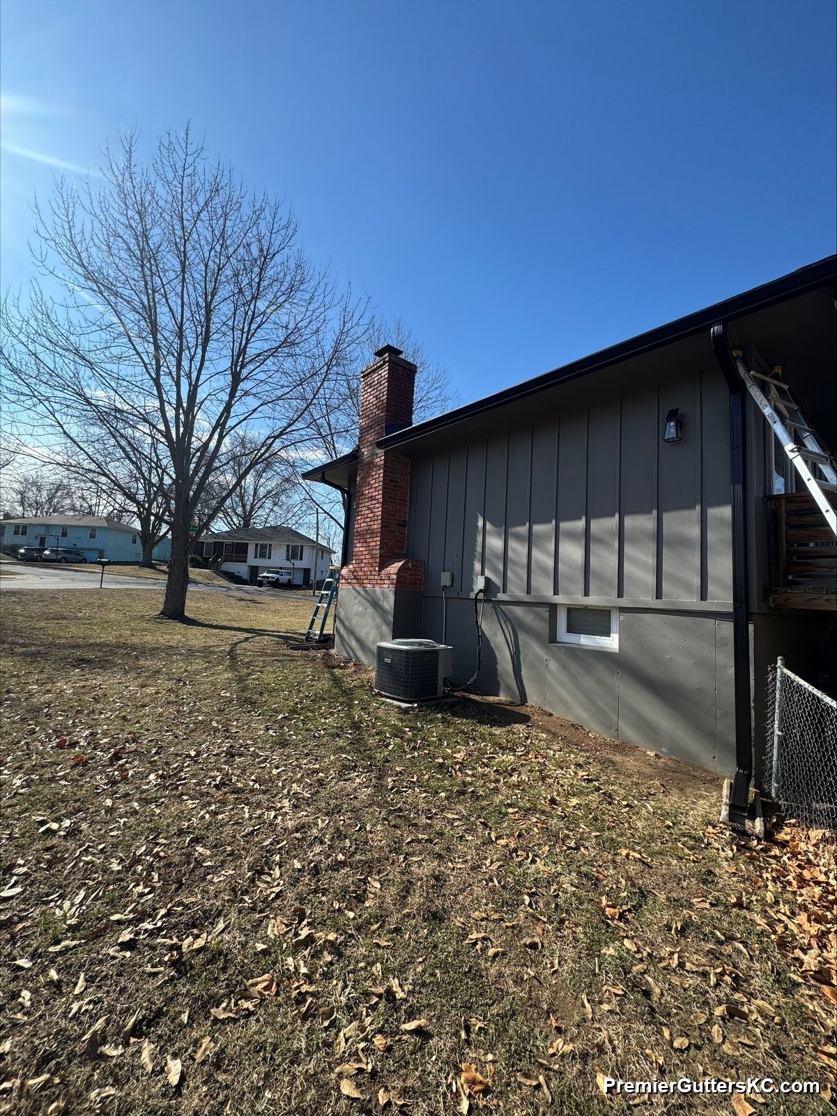Charcoal board-and-batten ranch home with black seamless gutters and a downspout draining away from the foundation, photographed in winter in the Kansas City metro