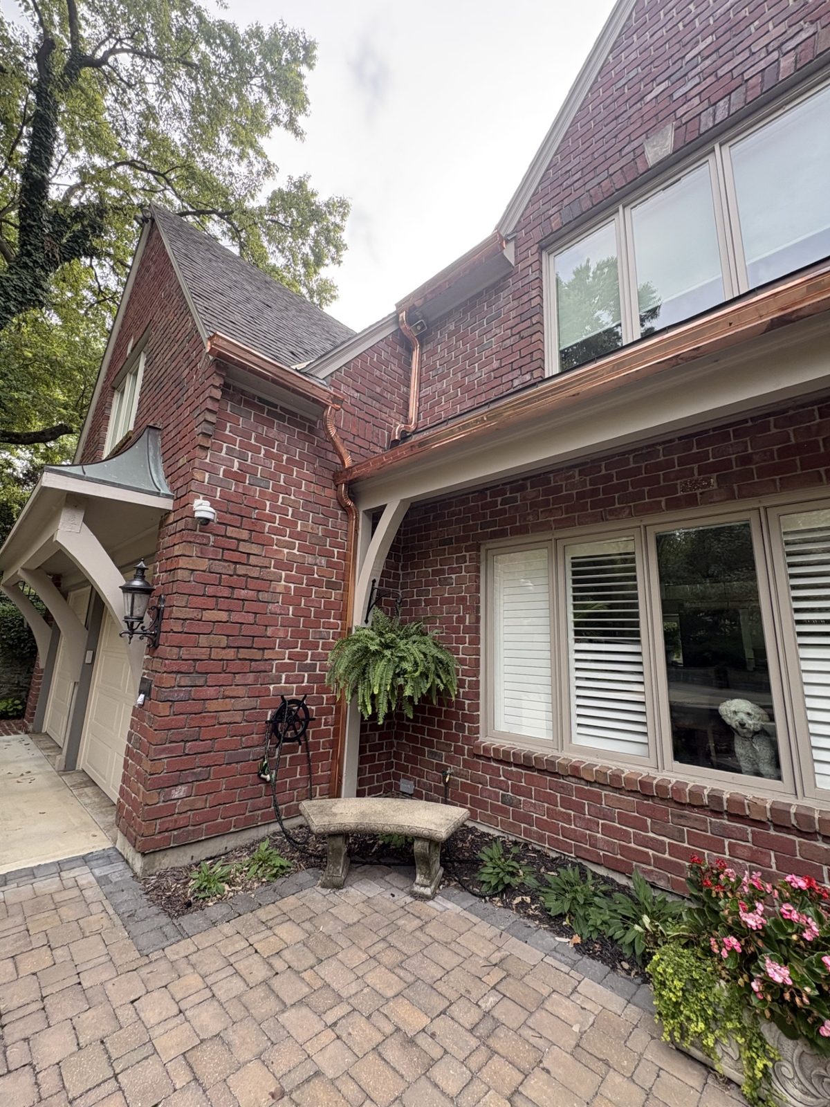 Close-up of a new copper gutter and copper downspout with a decorative offset elbow on a brick Tudor home in the Kansas City metro