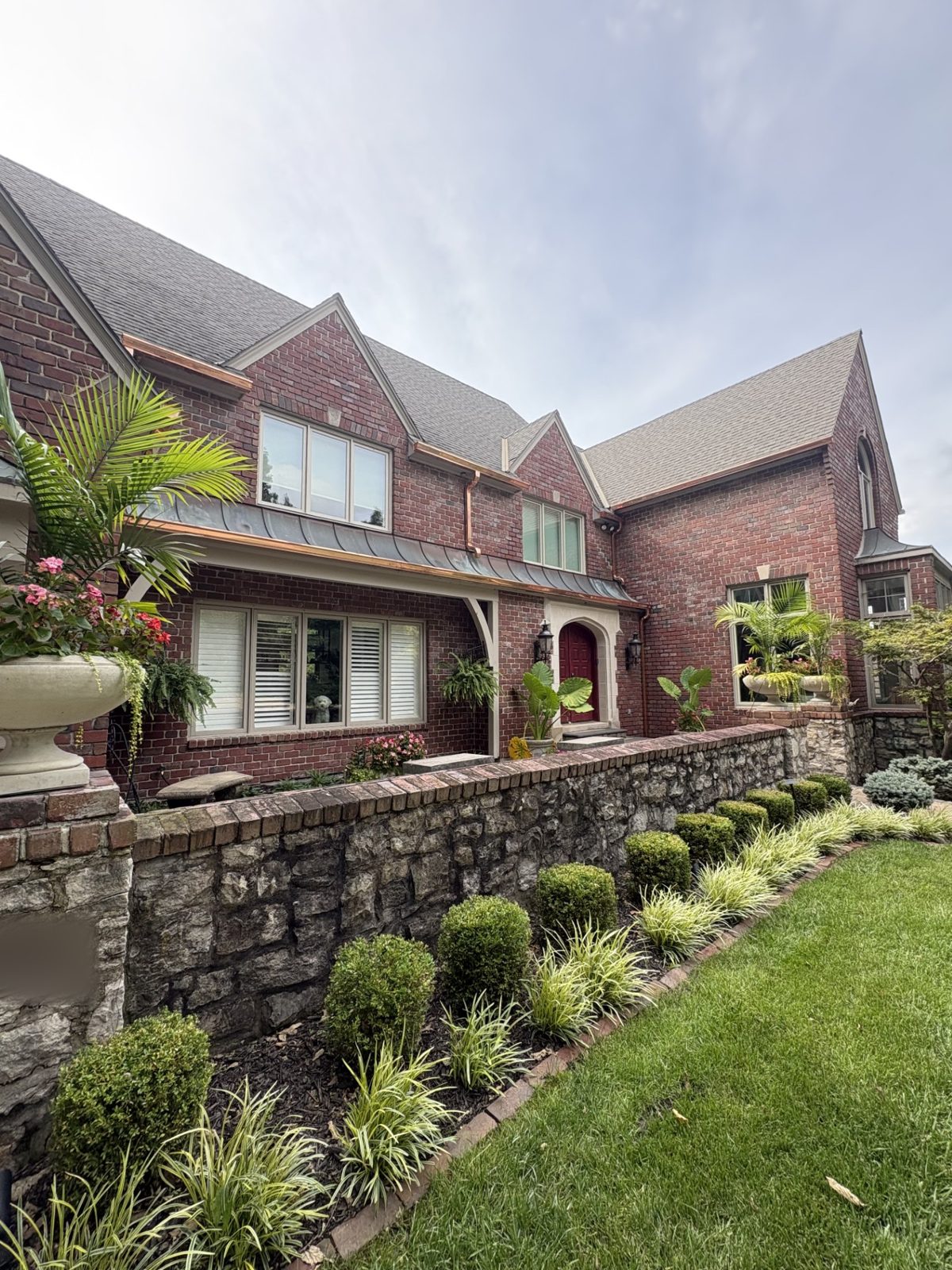 Angled view of copper gutters catching the light on a brick Tudor home with a stone courtyard wall in the Kansas City metro