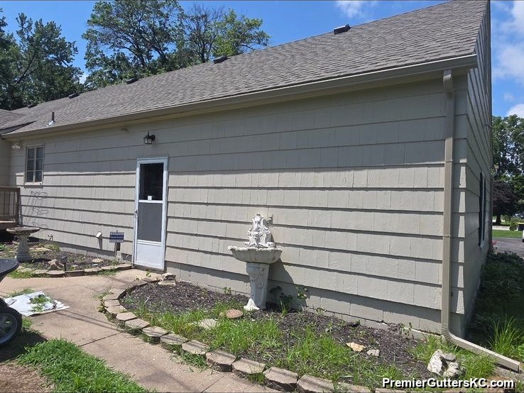 Side entry of a cream-sided ranch home with new white seamless gutters and a paver walkway in the Kansas City metro