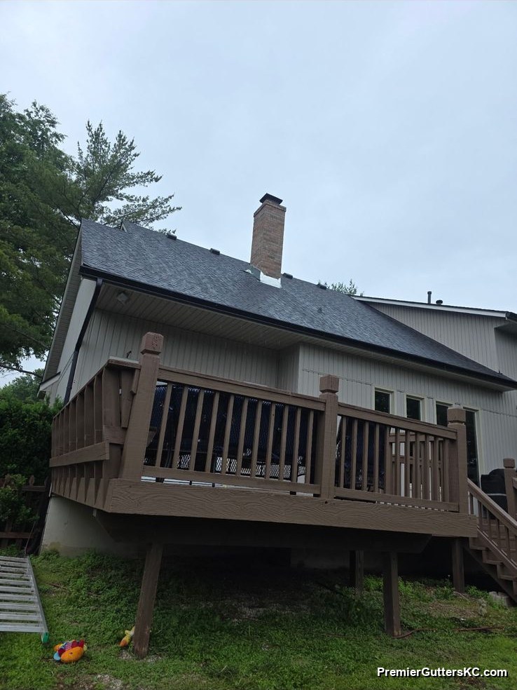 Gray two-tone home with a raised wood deck and white seamless gutters with a downspout routed neatly past the deck in the Kansas City metro