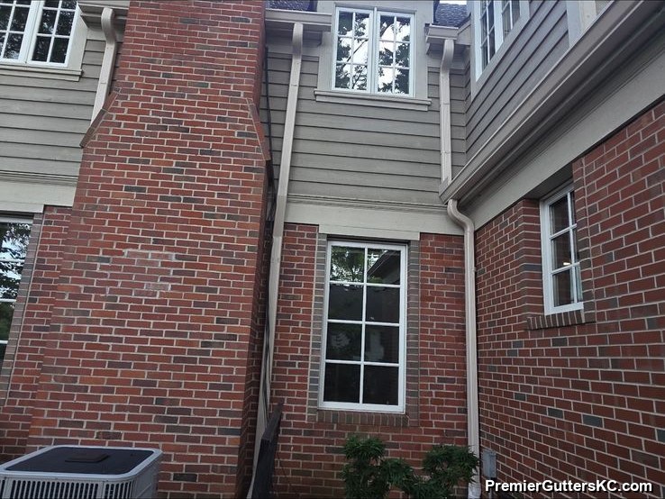 Two-story red brick colonial home with white seamless aluminum gutters and downspouts along the eaves and second-story windows in the Kansas City metro