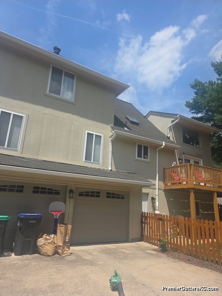 Sage-green stucco two-story home with an attached two-car garage and white seamless gutters with downspouts running to the driveway in the Kansas City metro