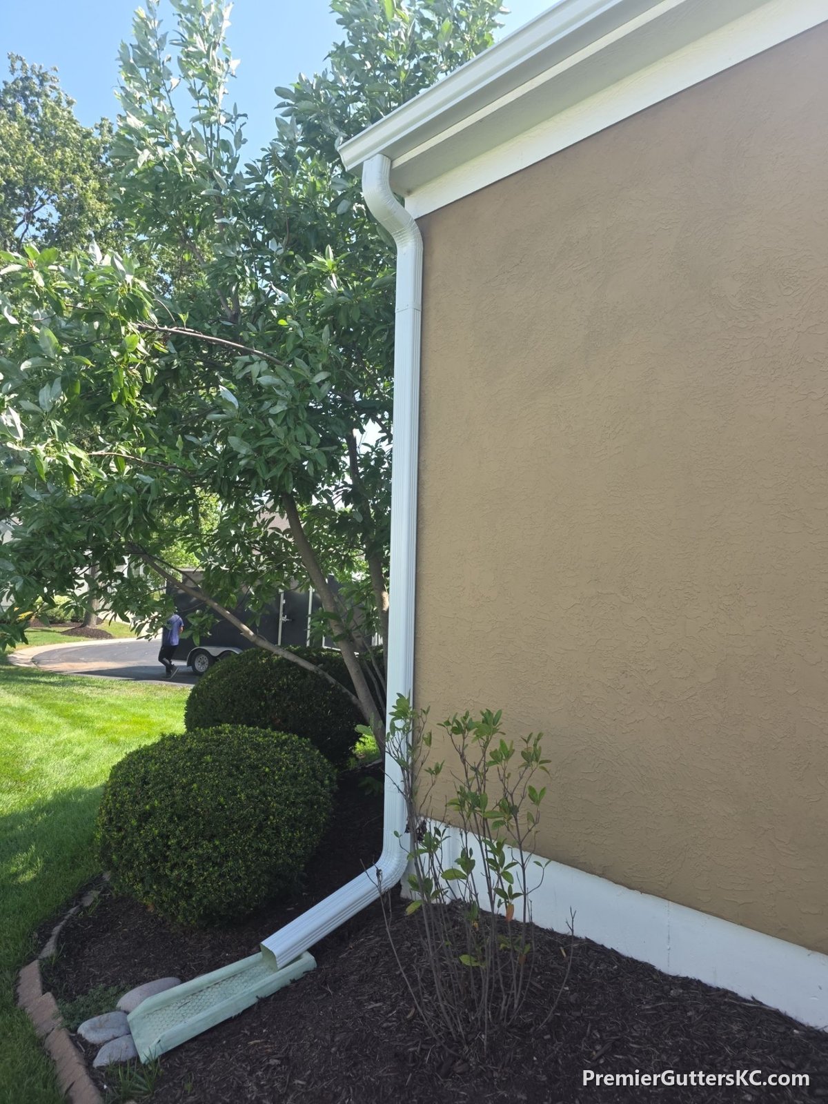 White seamless gutter and downspout draining to a splash block on a stucco home in Overland Park, Kansas