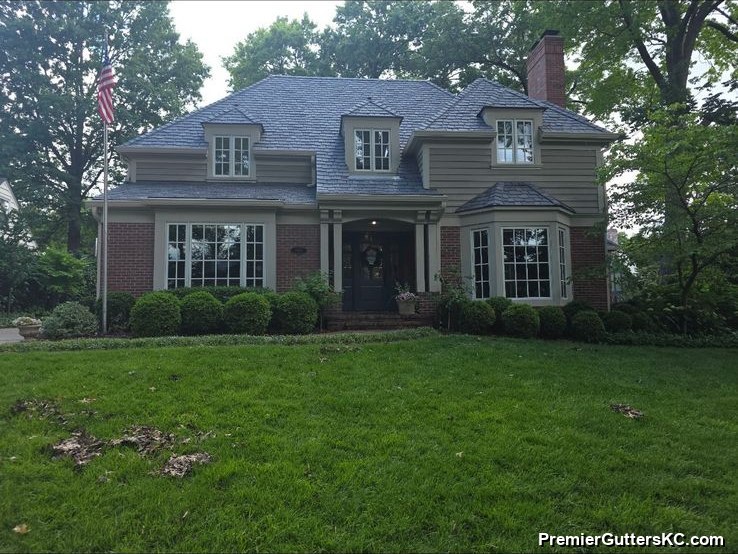 Stately two-story brick home with steep gables and white seamless gutters, set back on a large manicured lawn with mature trees in the Kansas City metro