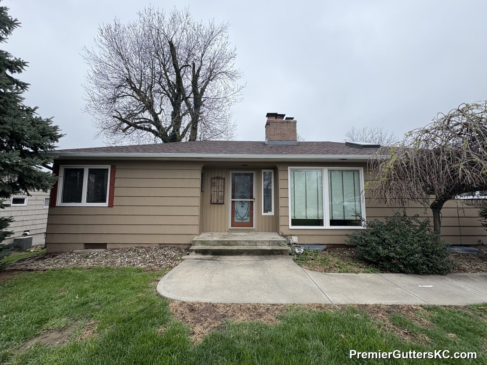 Tan brick ranch home with a large picture window and fresh white seamless gutters above the garage and front entry in the Kansas City metro
