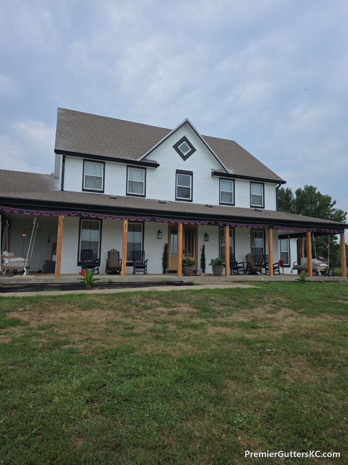 White farmhouse with wraparound porch and new black seamless gutters in Napoleon, Missouri