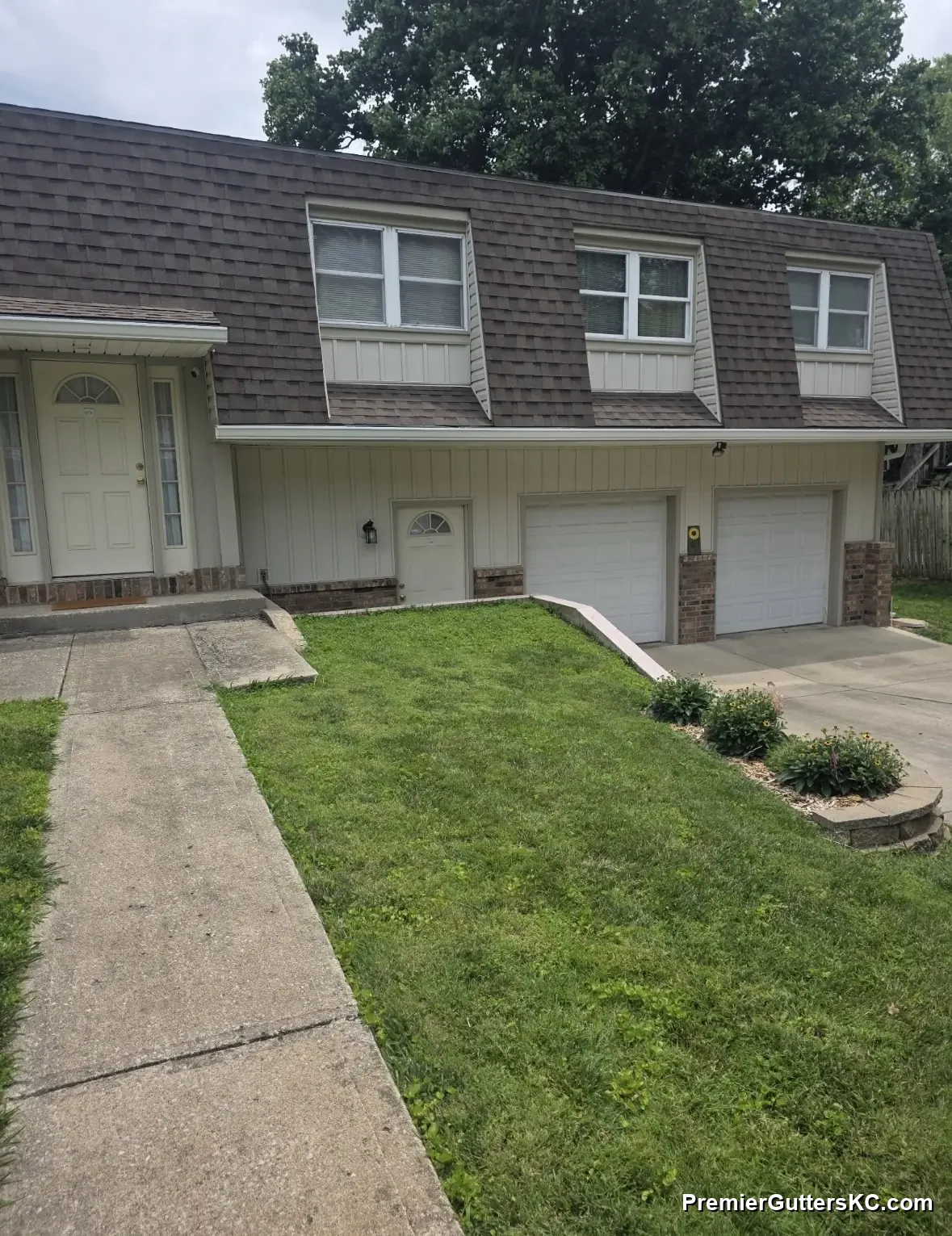 White seamless gutters and downspout on a brick townhome with dormer windows and a two-car garage in Overland Park, KS, installed by Premier Gutters KC